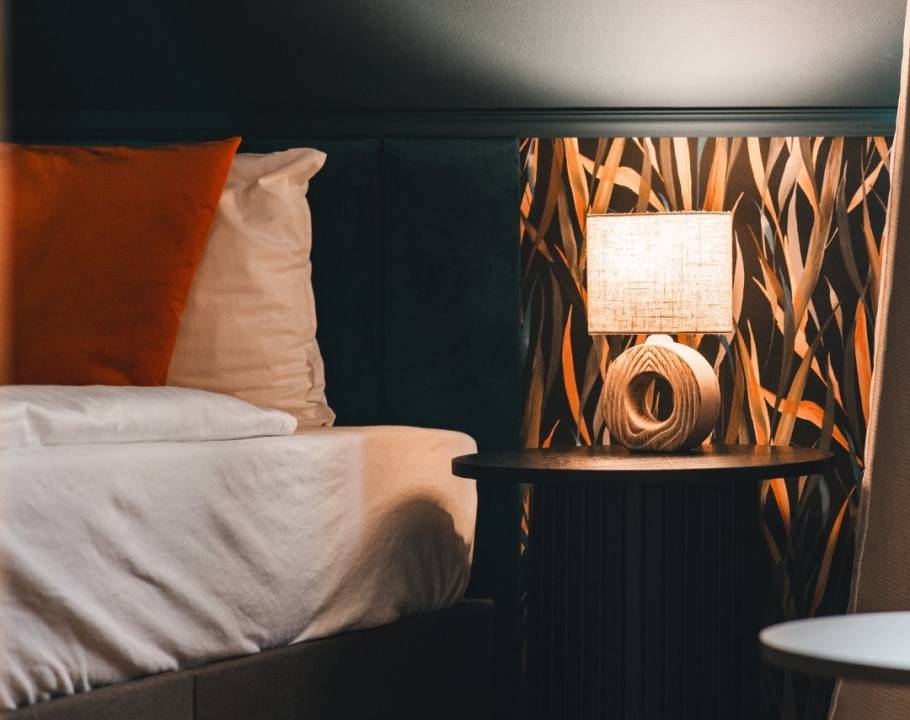 Teilansicht eines renovierten Hotelzimmers im Hotel Hüttmann mit modernem Design, gepolstertem Kopfteil und pastellgrüner Nachttischlampe