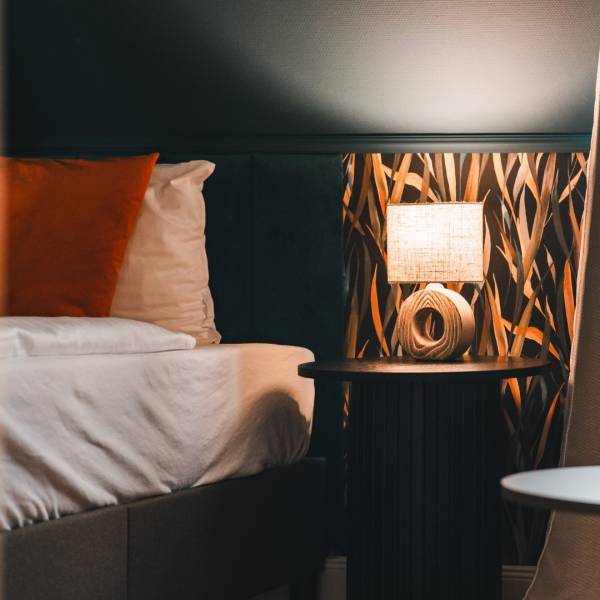 Teilansicht eines renovierten Hotelzimmers im Hotel Hüttmann mit modernem Design, gepolstertem Kopfteil und pastellgrüner Nachttischlampe