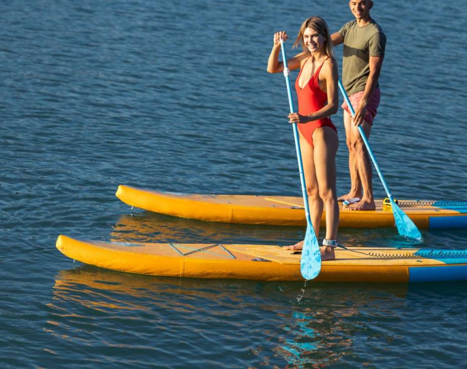 Mann und Frau paddeln nebeneinander auf gelben SUP-Boards auf einem stillen Gewässer